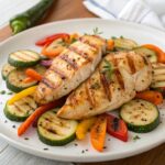 Colorful plate featuring grilled chicken breasts served with roasted bell peppers, zucchini, and carrots, garnished with fresh herbs.Healthy Grilled Chicken with Roasted Vegetables