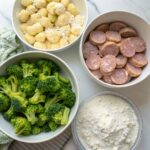 Gnocchi, sliced sausage, and broccoli florets on a platter, ready to be seasoned and roasted for a quick sheet pan dinner.