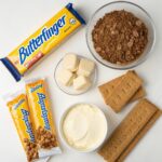 All ingredients for making Butterfinger Pie, including candy bars, cream cheese, and graham cracker crumbs