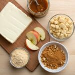Ingredients for Caramel Apple Cheesecake Bars including cream cheese, apples, caramel sauce, graham cracker crumbs, and nuts