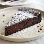 Flourless chocolate cake slice on a plate with a dusting of powdered sugar.